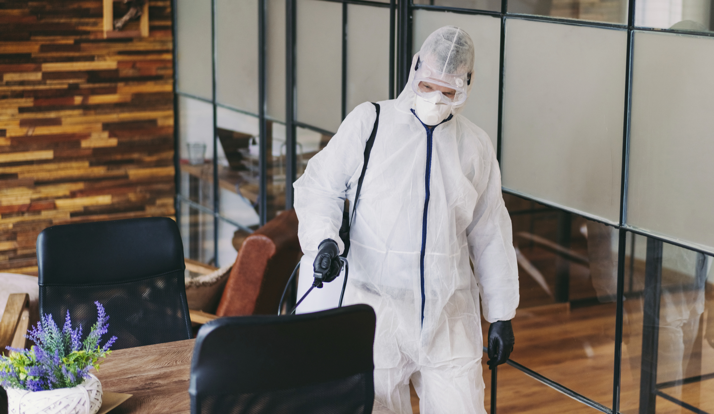 Man in protective suit and face mask spraying for disinfection in the office